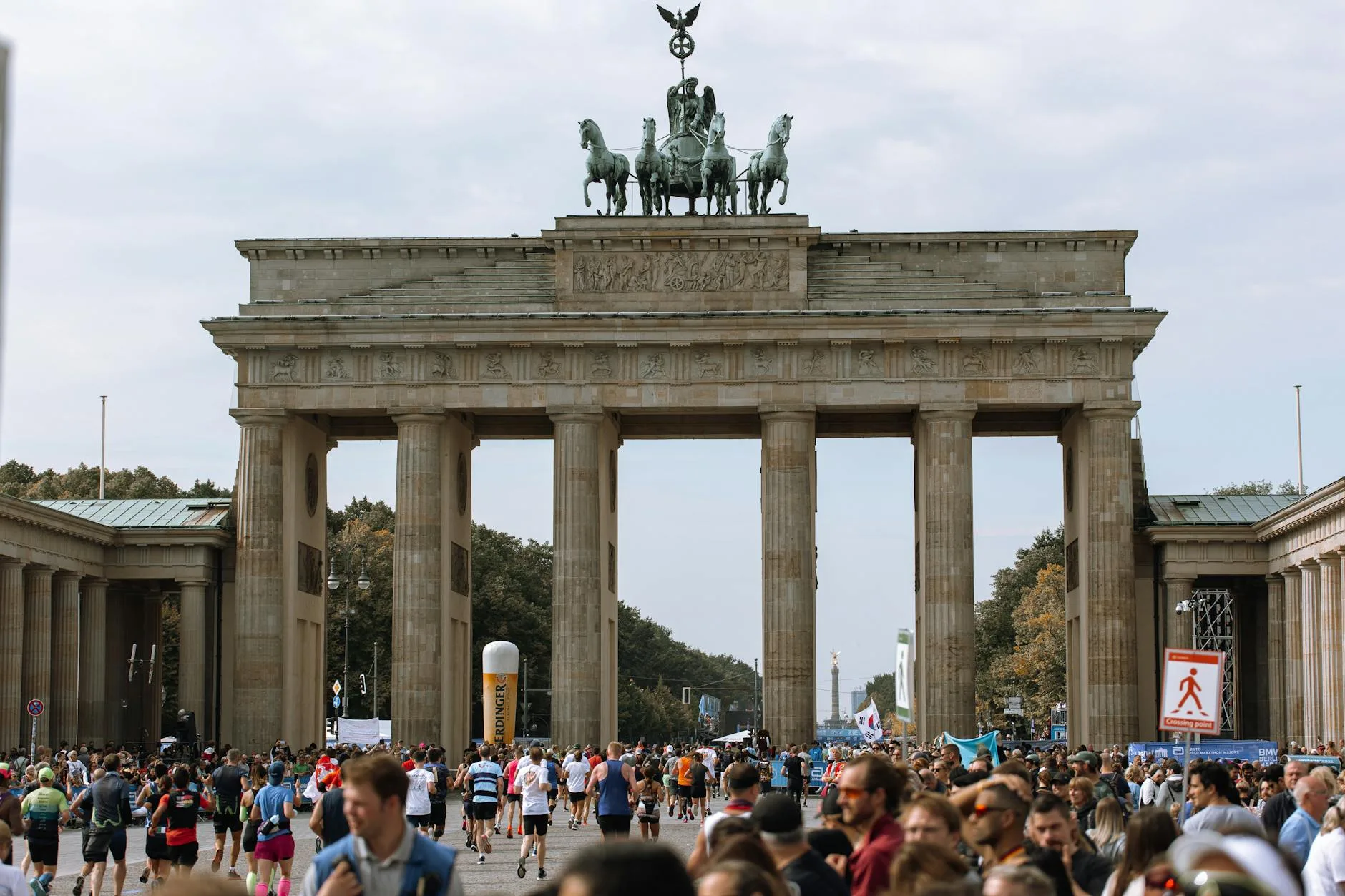 Runners crossing Berlin Marathon finish line past Brandenburg Gate at dawn