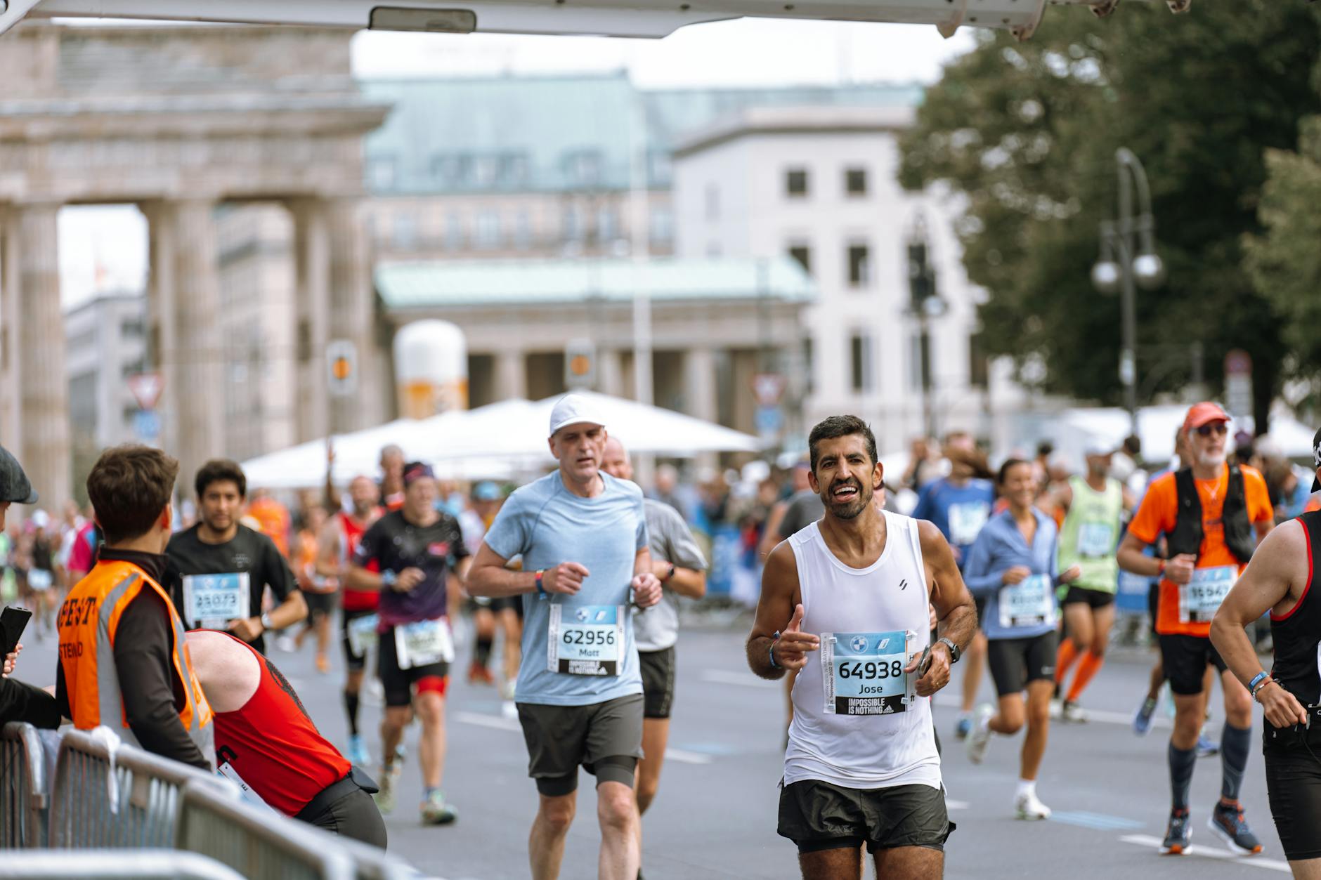 Runner crossing marathon finish line with arms raised in triumph, race bib visible