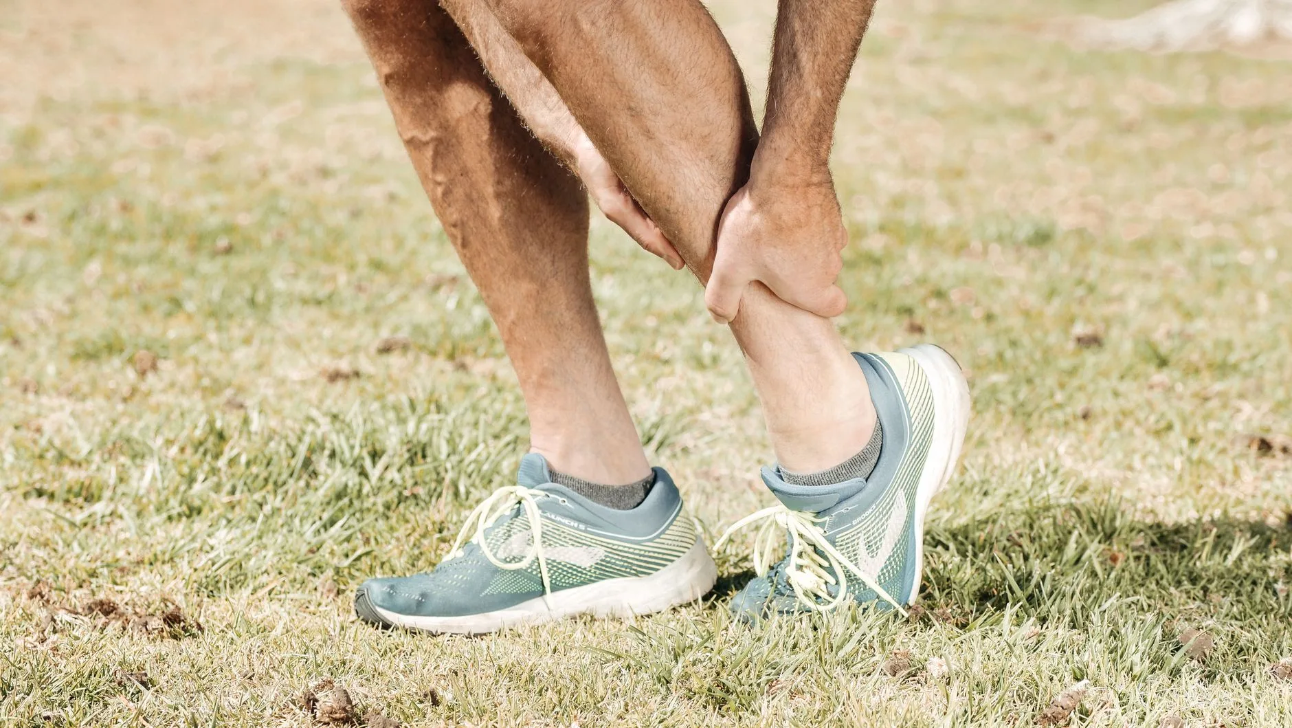 Runner clutching back of thigh in pain during outdoor run, showing hamstring strain