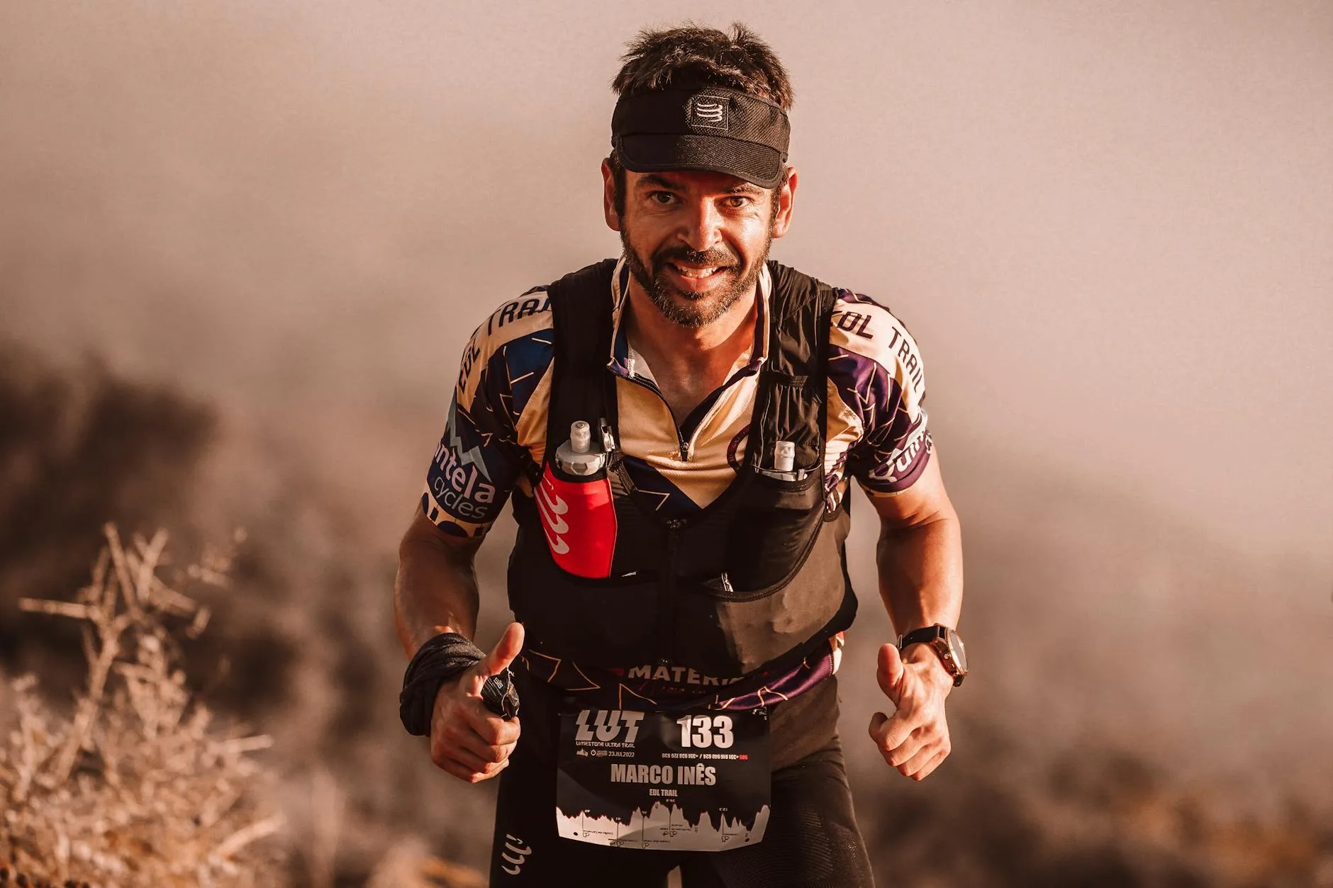 Runner on mountain trail at sunrise, backpack on, pushing uphill through rugged terrain.