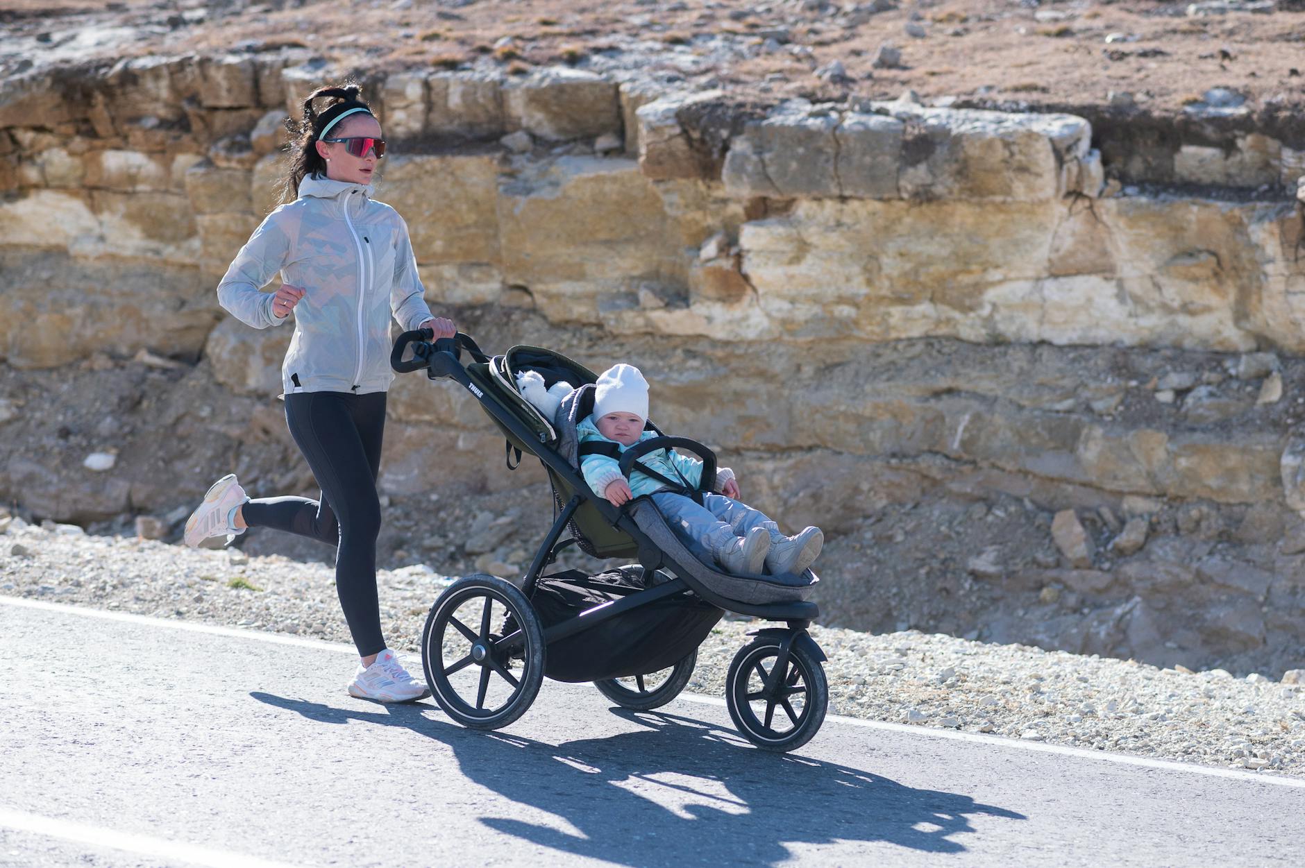 Mother jogging outdoors with baby stroller on a sunny park path