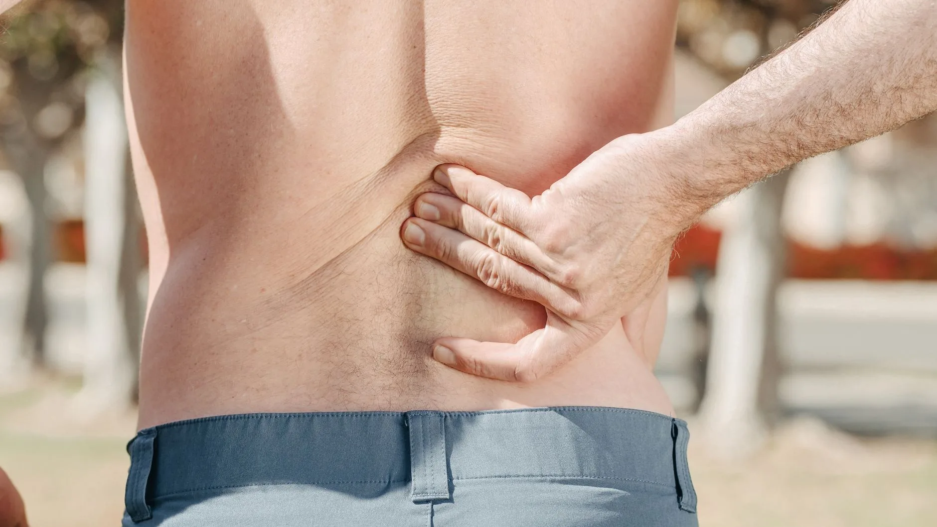 Runner clutching lower back in pain while jogging on outdoor path