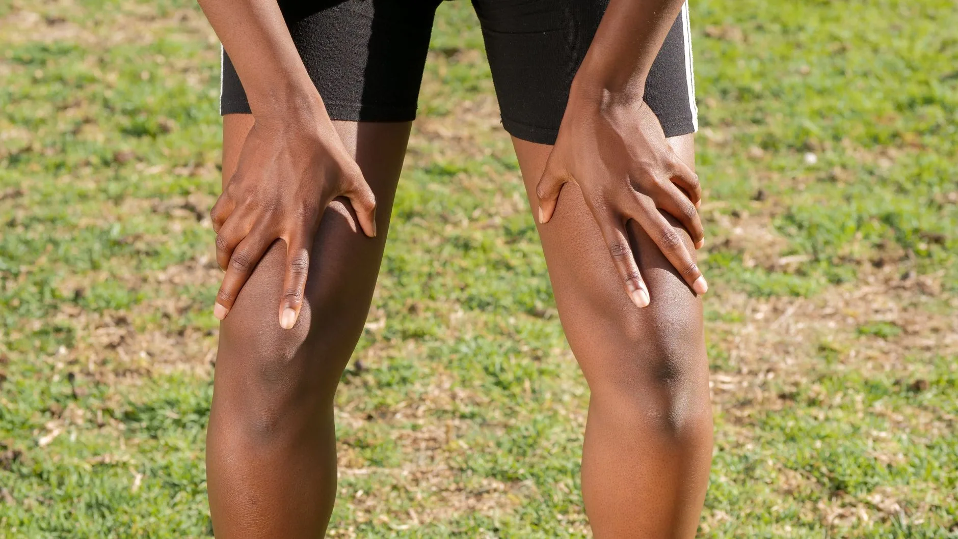 Runner clutching sore knee mid-stride on outdoor trail path